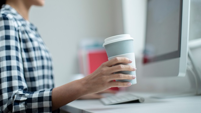 person holding a reusable coffee cup and entering data on a computer